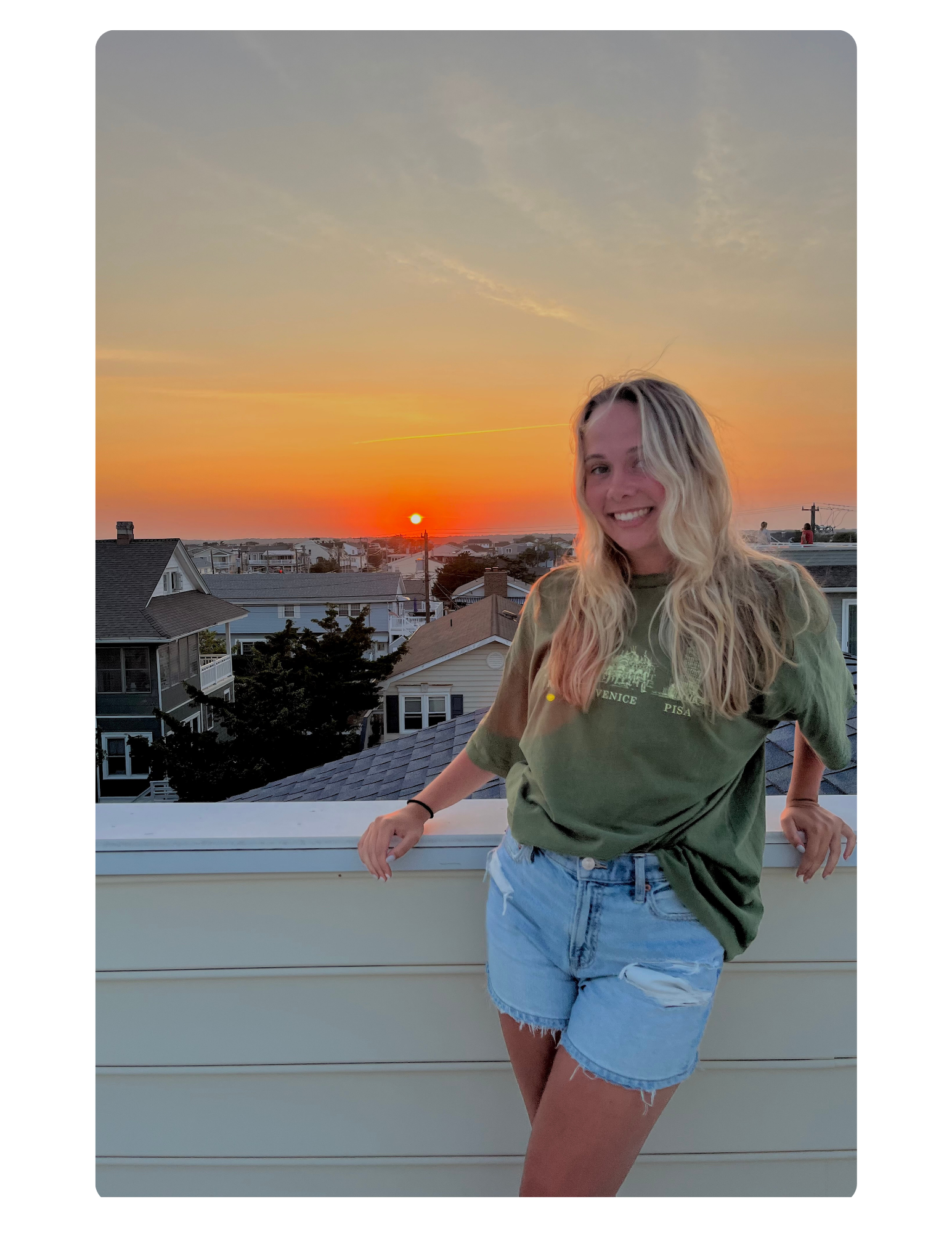 AnnE Potter, a girl with long blonde hair wearing a green t shirt and blue jean shorts leaning up against a balcony with a sunset in the background.